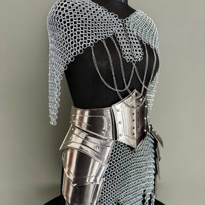 May include: A silver-colored chainmail and metal armor set displayed on a black mannequin. The armor includes a chainmail cape, a metal breastplate, and metal leg armor. Decorative chains hang from the chainmail.