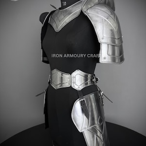 May include: Silver metal armor for the shoulders, waist, and thighs. The armor is made of metal plates and has a sleek, modern design. The armor is displayed on a black mannequin.