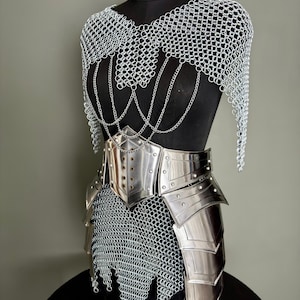 May include: A medieval-style armor set displayed on a black mannequin. The set includes a chainmail top with hanging chains, a silver metal belt, and metal plates. The armor is designed with a polished, reflective finish.
