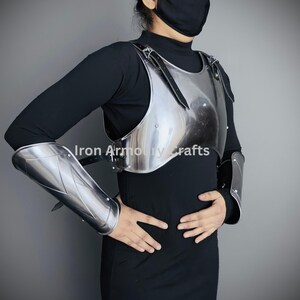 May include: A silver metal breastplate with shoulder straps and matching arm guards. The breastplate is worn over a black shirt.