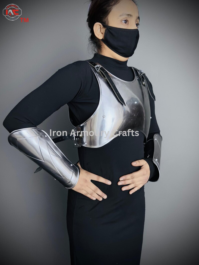 May include: A silver metal breastplate with shoulder straps and matching arm guards. The breastplate is worn over a black shirt.