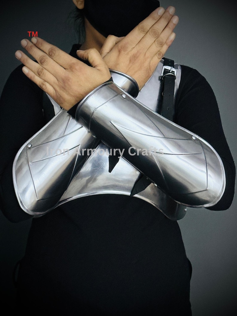 May include: A pair of silver metal arm guards with a decorative design. The guards are worn on the forearms and extend to the wrists.