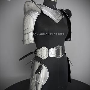 May include: Silver plated armor set for the torso, shoulders, and hips. The armor is made of metal plates and has a polished finish. The armor is displayed on a black mannequin. The text "IRON ARMOURY CRAFTS" is visible on the armor.