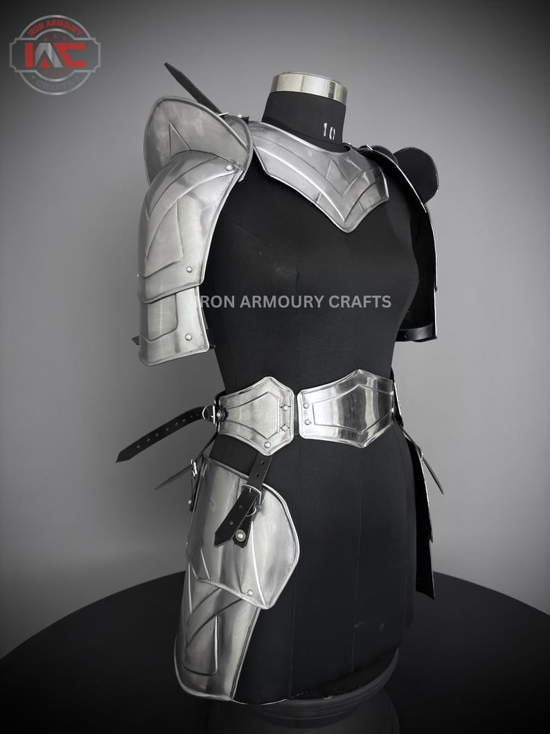 May include: Silver plated armor set for the torso, shoulders, and hips. The armor is made of metal plates and has a polished finish. The armor is displayed on a black mannequin. The text "IRON ARMOURY CRAFTS" is visible on the armor.