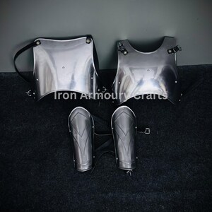 May include: A set of silver-colored medieval armor, including a chest plate, a breastplate, and two arm guards. The armor is laid out on a black surface. "Iron Armoury Crafts TM" is printed in the top left corner of the image.