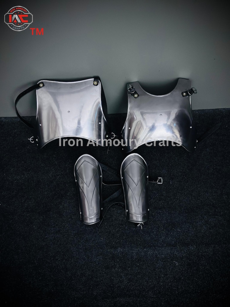 May include: A set of silver-colored medieval armor, including a chest plate, a breastplate, and two arm guards. The armor is laid out on a black surface. "Iron Armoury Crafts TM" is printed in the top left corner of the image.