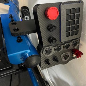 A black and gray racing simulator button panel with a red button, multiple black buttons, and a grid of 12 black buttons. The panel is mounted on a blue metal frame.