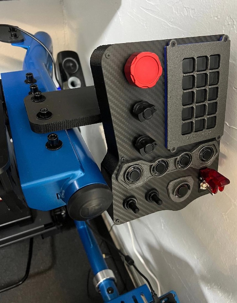 A black and gray racing simulator button panel with a red button, multiple black buttons, and a grid of 12 black buttons. The panel is mounted on a blue metal frame.