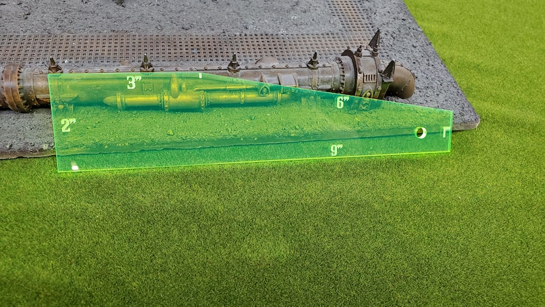 May include: A green ruler with markings in inches, measuring 9 inches long, 6 inches wide, and 3 inches high. The ruler is placed on a brown surface with a metal pipe and other objects.