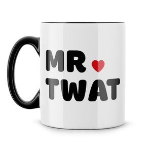 May include: White ceramic mug with a black handle and interior. The mug features the text "MR ❤️ TWAT" in bold black letters with a red heart symbol. The mug is designed for beverages.