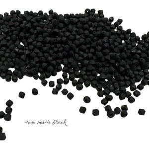 May include: A pile of 4mm matte black beads. The beads are small, faceted, and have a matte finish. The beads are scattered across a white background. The text "4mm matte black" is written in a cursive font.