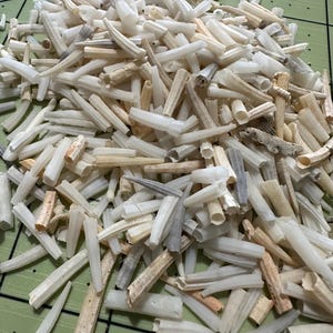 May include: A pile of small, hollow, cylindrical objects in varying shades of white, cream, and tan. The objects appear to be cut or broken, with some showing a textured surface. The background is a green cutting mat.
