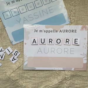 Può includere: Due fogli di attività stampabili per aiutare i bambini ad imparare a scrivere i loro nomi. Il primo foglio è blu e presenta il nome "YASSINE" con spazi vuoti per gli adesivi. Il secondo foglio è rosa e presenta il nome "AURORE" con tessere di lettere.