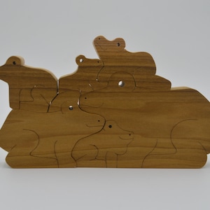 May include: A wooden puzzle featuring a group of frogs stacked on top of each other. The puzzle is made of natural wood and has a light brown color.