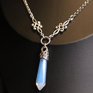 May include: A silver chain necklace with a delicate, ornate design. The necklace features a pendant with a light blue, faceted, teardrop-shaped stone.