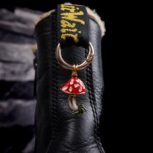May include: Black leather boot with a red and white mushroom charm attached to the black strap with the word "Dr. Martens" written in yellow.