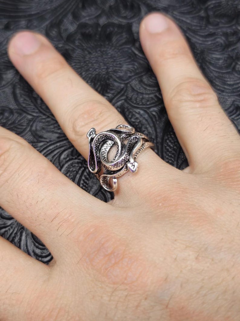 May include: A silver-colored ring featuring a detailed snake design. The snake is coiled around the finger, with intricate scales and a textured surface. The ring is a statement piece, perfect for those who appreciate unique jewelry.