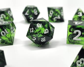 May include: A set of polyhedral dice featuring a translucent green resin base with swirling black ink patterns and crisp white numbers. The collection includes various geometric shapes such as a twenty-sided die, a cube, and pyramids, all displaying high-contrast numerals.