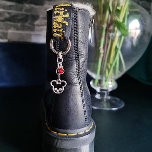 May include: Black leather boots with a yellow pull tab and a silver charm with a red gem. The boots have a thick black sole.