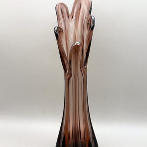 May include: A tall, translucent mauve glass vase with a flared, organic rim featuring multiple petal-like points. The body of the vase is characterised by vertical, ribbed fluting that extends from the base up to the irregular, open top.