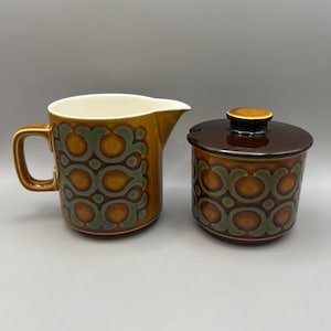 May include: A brown and green ceramic creamer and sugar bowl set with a geometric pattern.