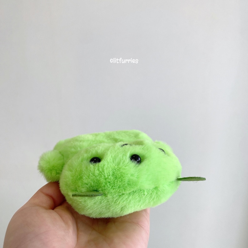 May include: A bright lime green plush toy with a soft, fuzzy texture, two small black bead eyes, and two thin green felt antennae protruding from the top. The text clitfurries is printed in small white letters above the plush object.