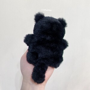 May include: Black plush cat toy with a long tail. The cat is sitting up with its back to the camera.