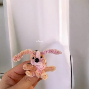 Puede incluir: Un juguete para perro de limpiapipas rosa y naranja con ojos negros. El juguete está hecho a mano y tiene un aspecto caprichoso y de dibujos animados.
