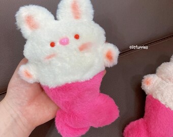 May include: A white plush bunny with pink ears and a pink tail. The bunny has a pink and white mermaid tail.
