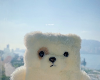 May include: A plush white bear toy with a fuzzy texture, featuring two black eyes, a black nose, and a small brown patch over the right eye. The text litfurries is printed in small white letters above the bear's head against a bright sky.