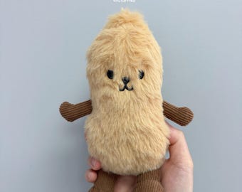 Puede incluir: Un pequeño peluche con cuerpo de pelaje beige y brazos y piernas de pana marrón. La cara presenta ojos y una boca pequeña bordados en negro. El texto "clitfurries" está impreso en letras blancas pequeñas sobre la cabeza del peluche.