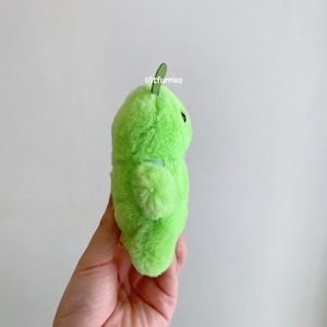 May include: A bright lime green plush toy with a soft, fuzzy texture, a small dark green leaf-like protrusion on top, and a single visible black eye. The text "litfurries" is printed in white on the upper portion of the plush surface.