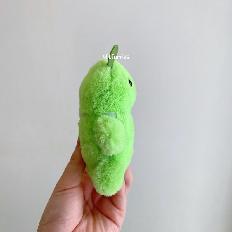 May include: A bright lime green plush toy with a soft, fuzzy texture, a small dark green leaf-like protrusion on top, and a single visible black eye. The text "litfurries" is printed in white on the upper portion of the plush surface.