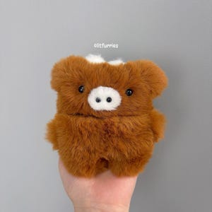 May include: A plush, fuzzy brown animal-shaped case with a white snout and small black eyes. The text litfurries is printed in white above the object. The item features a soft, textured surface and a rounded, compact design with two small ears.