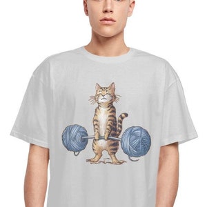 Könnte beinhalten: Ein weißes T-Shirt mit einer Cartoon-Illustration eines Tabby-Katers, der zwei Wollknäuel mit einer Langhantel hochhebt.