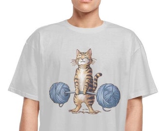 May include: A white t-shirt with a cartoon illustration of a tabby cat lifting two balls of yarn with a barbell.