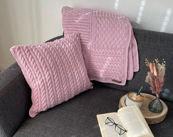 Könnte beinhalten: Ein graues Sofa mit zwei rosa gestrickten Kissen und einer rosa gestrickten Decke. Ein Buch, eine Brille und eine Tasse Kaffee stehen auf einem Holztablett auf dem Sofa.