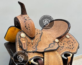 May include: A brown leather saddle with intricate floral tooling and a black leather seat. The saddle is on a wooden stand and has a white and brown stirrup. The saddle is labeled "Optimum Leather Stock Horse Saddles".