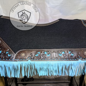 May include: Black saddle pad with turquoise fringe and brown leather trim. The leather trim features a floral design and silver accents. The saddle pad is labelled "Optimum Leather Stock Horse Saddles".