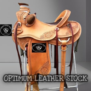 May include: A brown leather saddle with intricate tooling and a saddle horn. The saddle is on a metal stand and has a "OPTIMUM LEATHER SEAT" brand on the flap.