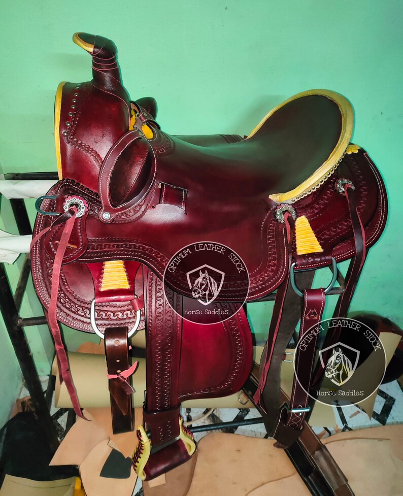 K&ouml;nnte beinhalten: Ein brauner Ledersattel f&uuml;r Pferde mit gelben N&auml;hten und einem Sattelhorn. Der Sattel ist mit einem gepr&auml;gten Lederdesign verziert und hat einen Metallsteigb&uuml;gel. Der Sattel ist mit "Optimum Leather Stock Horse Saddles" beschriftet.