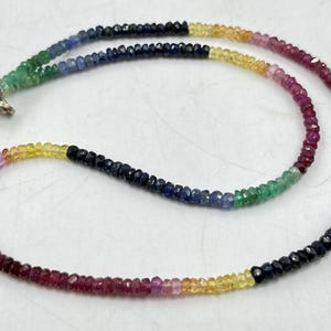 Op de afbeelding: Een veelkleurige edelsteenketting met rode, roze, gele, groene en blauwe kralen. De ketting is gemaakt van kleine, gefacetteerde kralen en heeft een zilveren sluiting.