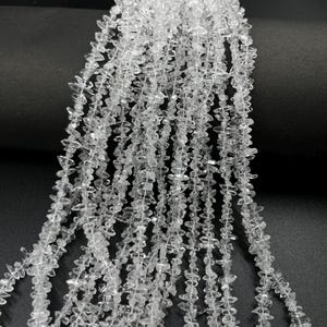 Peut inclure: Plusieurs brins de perles en cristal de quartz brut, transparentes et de forme irrégulière. Chaque brin présente de petits éclats de pierre translucides, dentelés et enfilés, créant un aspect texturé et réfléchissant aux bords anguleux.