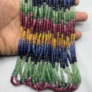 Op de afbeelding: Een verzameling veelkleurige edelsteen kralen, waaronder tinten groen, blauw, rood en geel. De kralen zijn aan elkaar geregen, waardoor een gelaagd effect ontstaat. De edelstenen zijn klein en facetgeslepen, waardoor ze licht reflecteren.