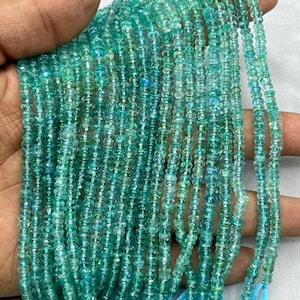May include: A strand of teal blue apatite beads, faceted and round, with a light green hue. The beads are strung on a thin thread and have a tassel at the end.