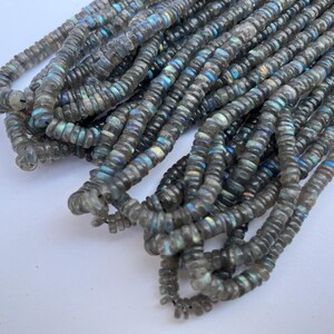 May include: A strand of gray labradorite gemstone beads. The beads are faceted and have a iridescent sheen.