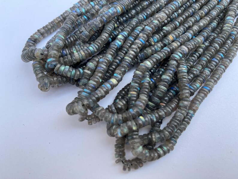 May include: A strand of gray labradorite gemstone beads. The beads are faceted and have a iridescent sheen.