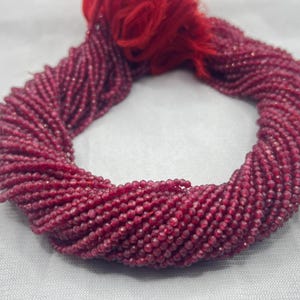 May include: A strand of deep red ruby beads, faceted and polished, strung together for jewelry making. The beads are small and uniform in size, creating a delicate and elegant look.