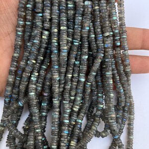 May include: A strand of dark gray labradorite gemstone beads. The beads are faceted and have a shimmering iridescent effect. The beads are approximately 6mm in size.