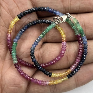 Puede incluir: Un collar de piedras preciosas multicolores con un cierre de plata. El collar presenta cuentas redondas de piedras preciosas rojas, amarillas, verdes y azules.